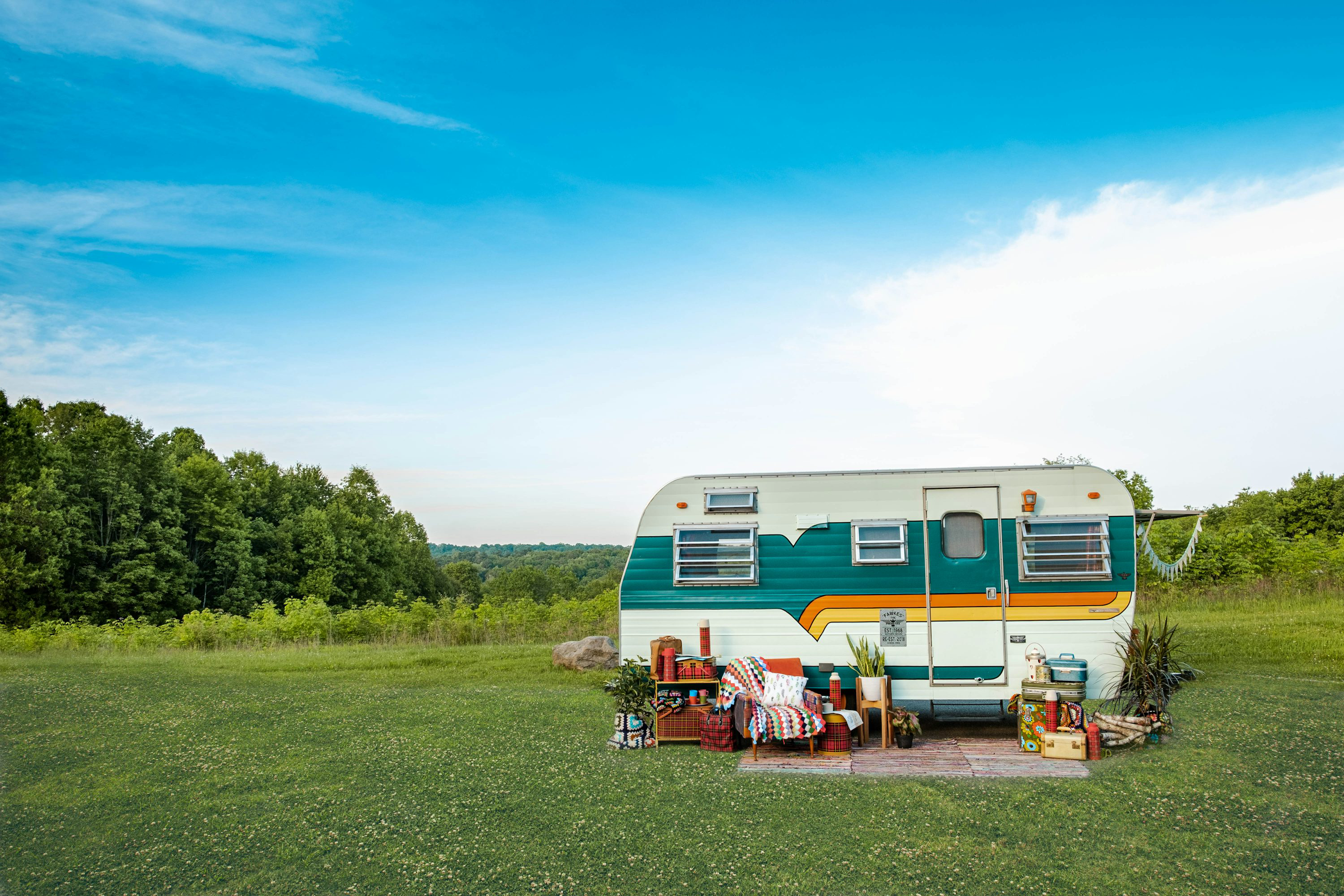 White and blue travel trailer parked in a sunny green field